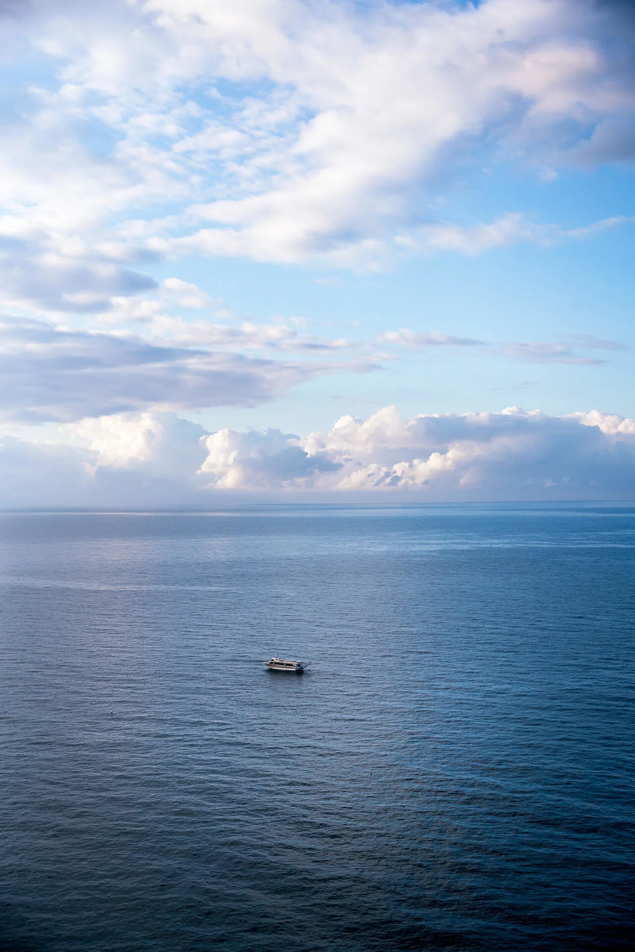 Barca solitaria su un mare calmo sotto un cielo parzialmente nuvoloso.