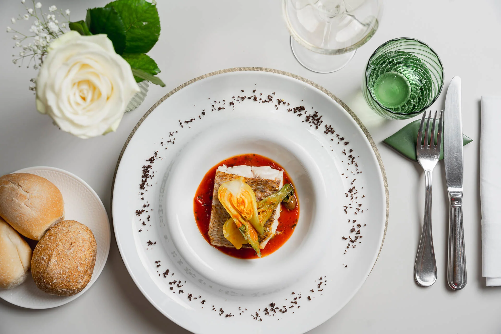 Piatti di pesce gourmet con decorazioni floreali e pane su tavola elegante.