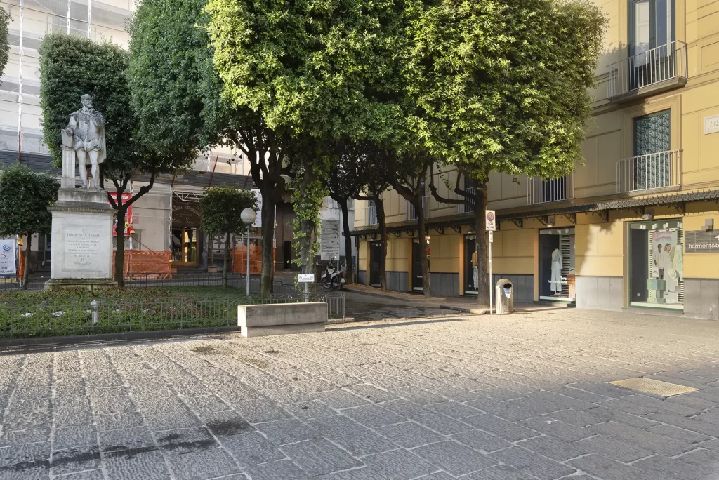 Statua di Torquato Tasso in una piazza alberata con edifici sullo sfondo.