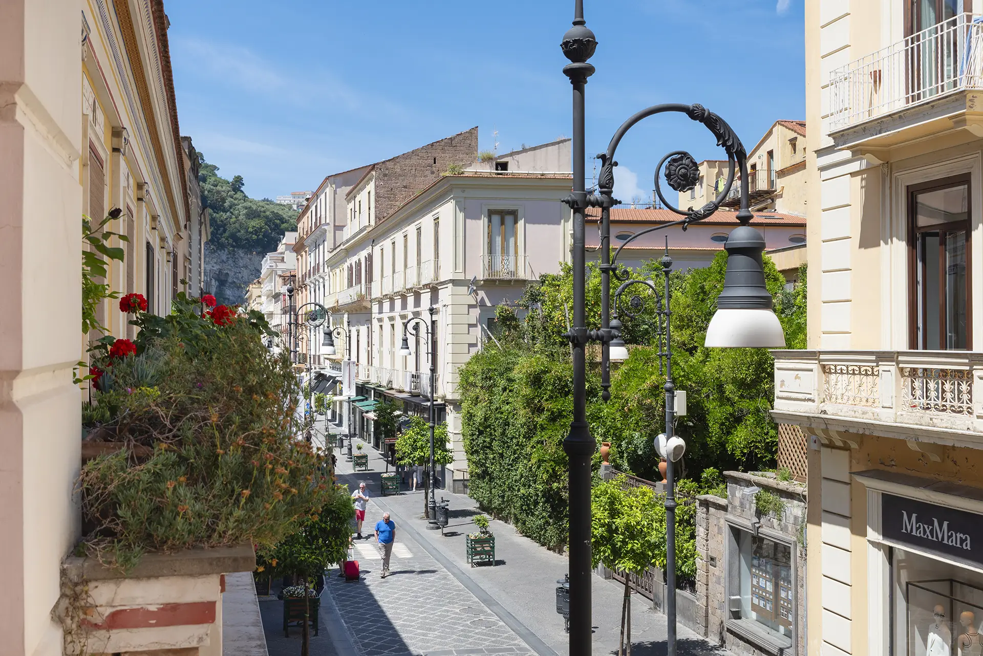 Strada alberata con edifici storici e lampioni eleganti in una città soleggiata.
