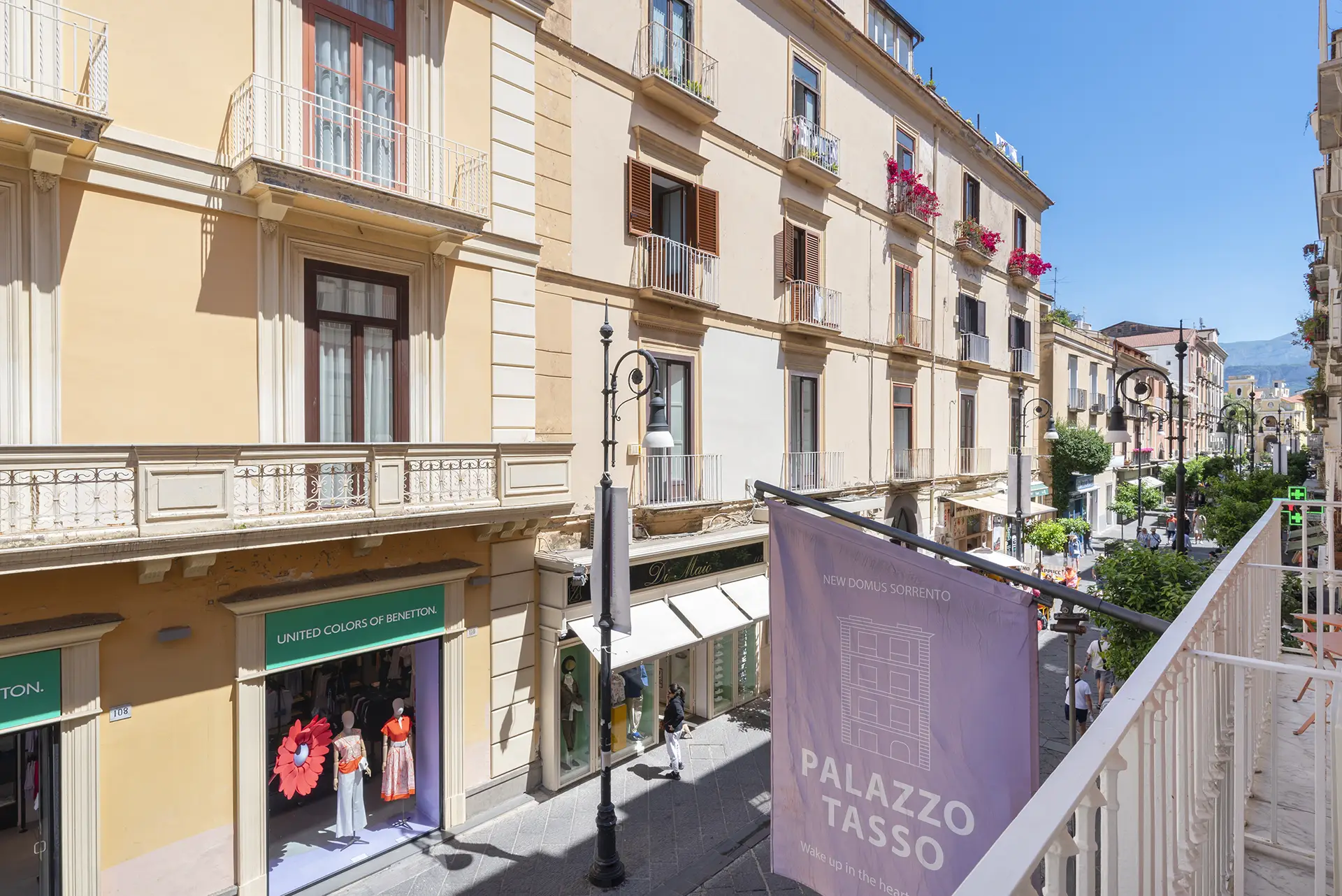 Street view of a sunny European city with shops and balconies.