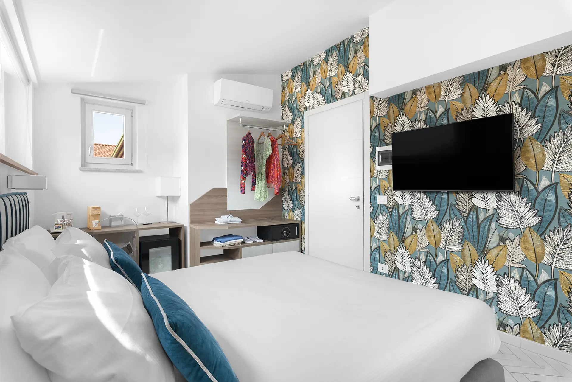 Camera d'albergo luminosa e moderna con letto matrimoniale, carta da parati floreale e TV a parete.
