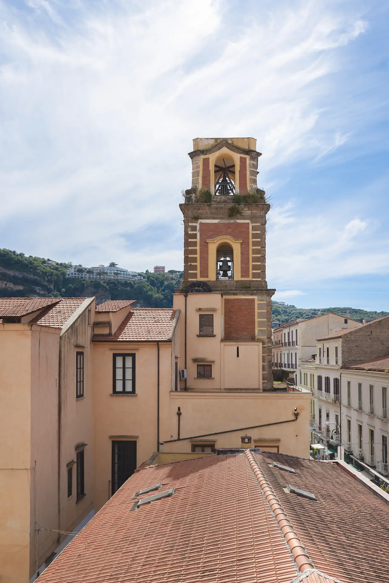 Campanile di una chiesa storica con tetti in tegole e un cielo azzurro sullo sfondo.