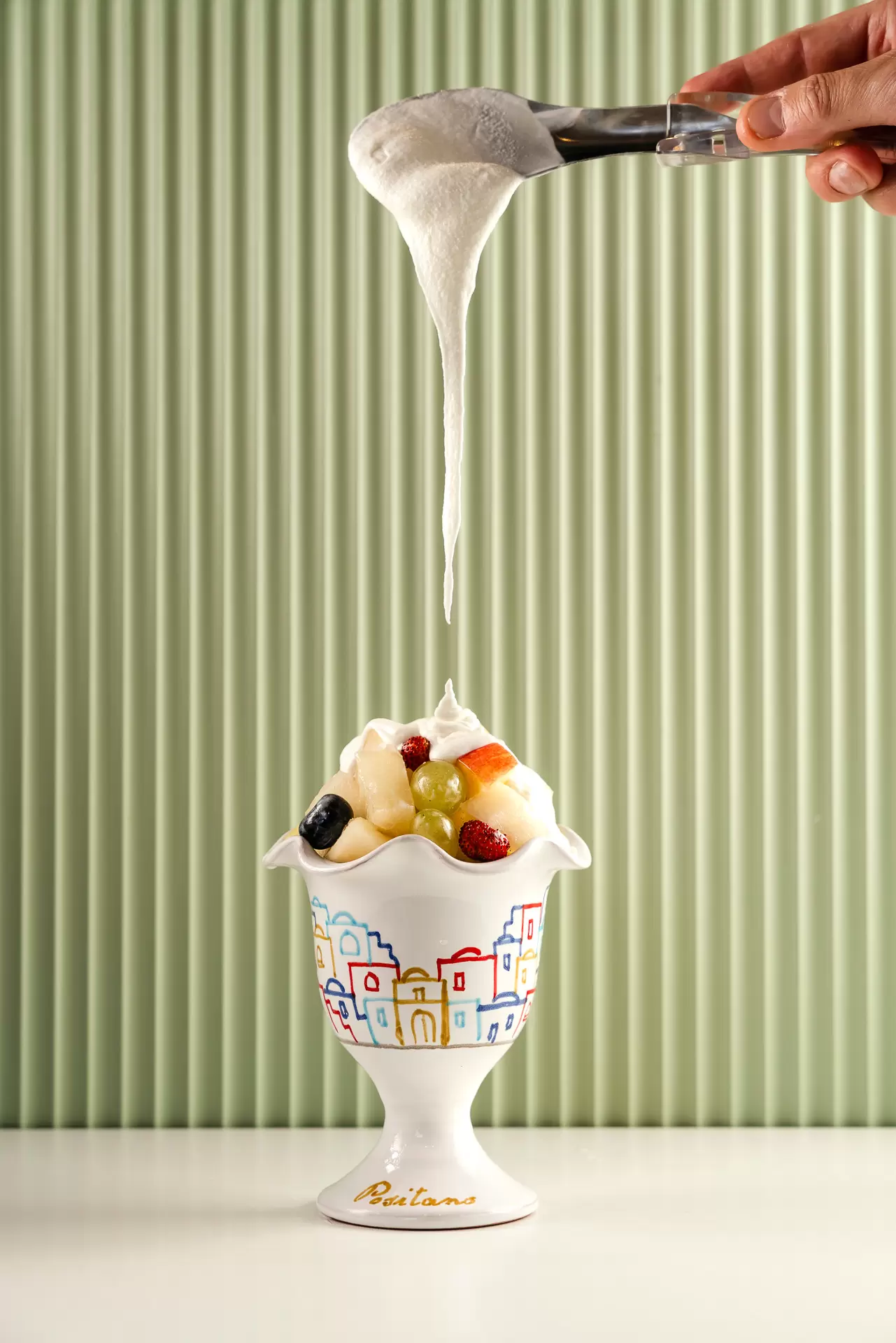 Coppetta di frutta mista con panna che cola da un cucchiaio sopra di essa.