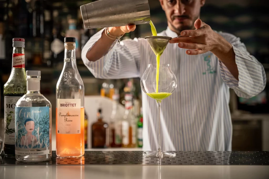 Bartender che prepara un cocktail verde setacciato in un bicchiere di design.