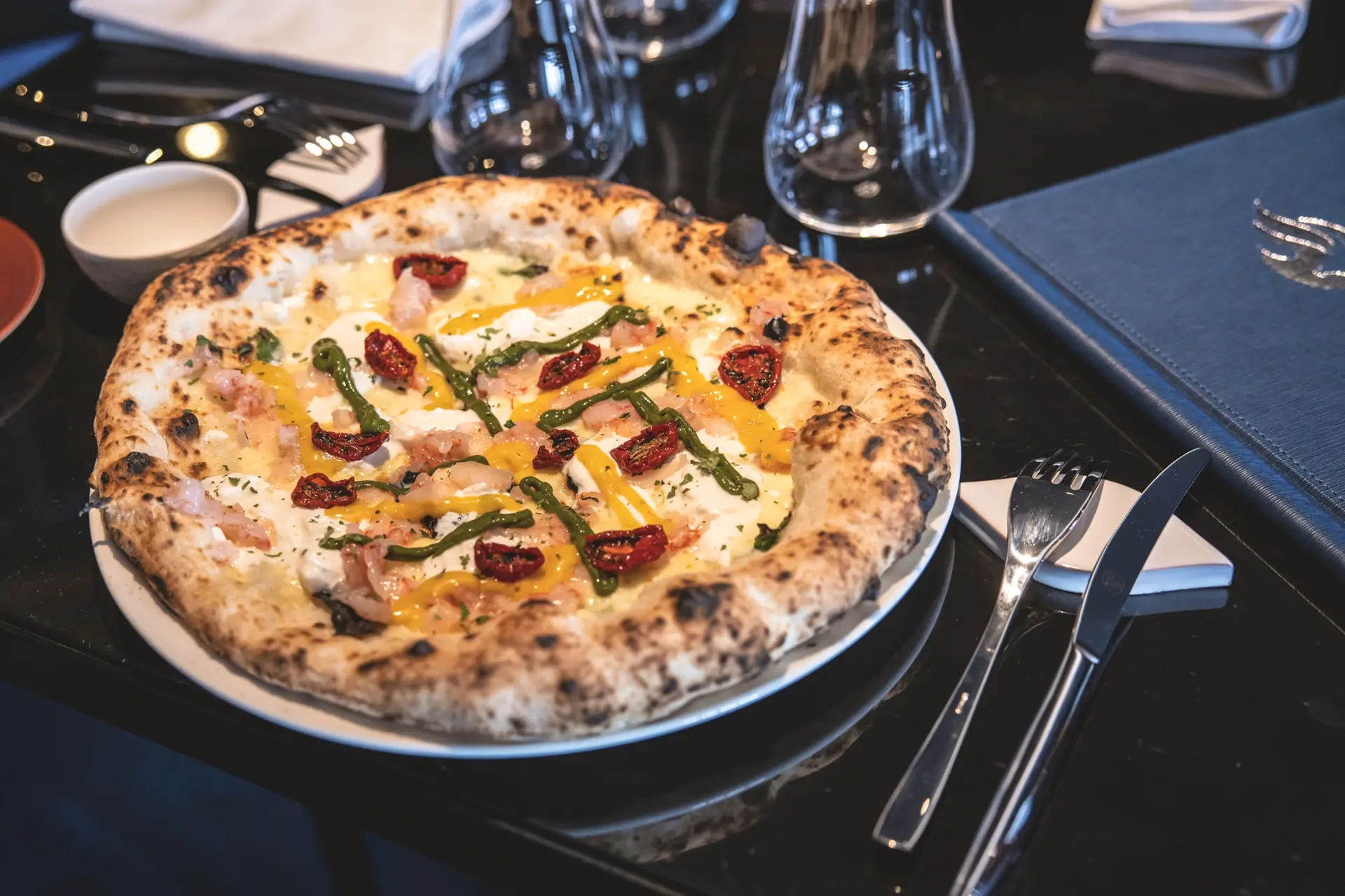 Pizza gourmet con pomodorini, prosciutto e crema su un tavolo apparecchiato.