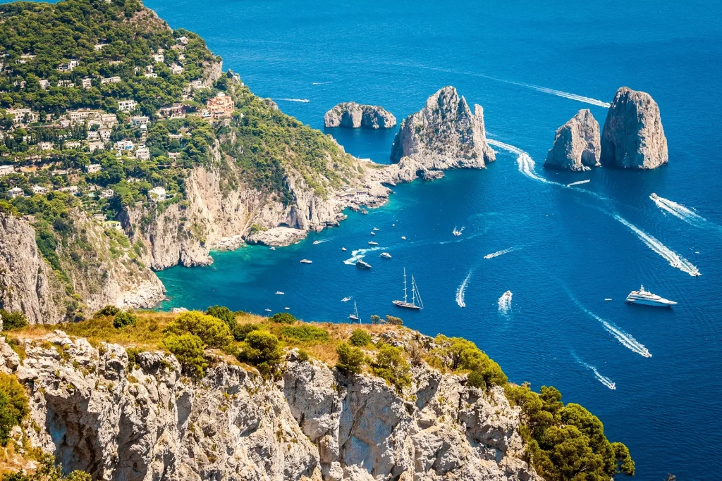 Vista panoramica dei Faraglioni di Capri con il mare blu e barche a vela.