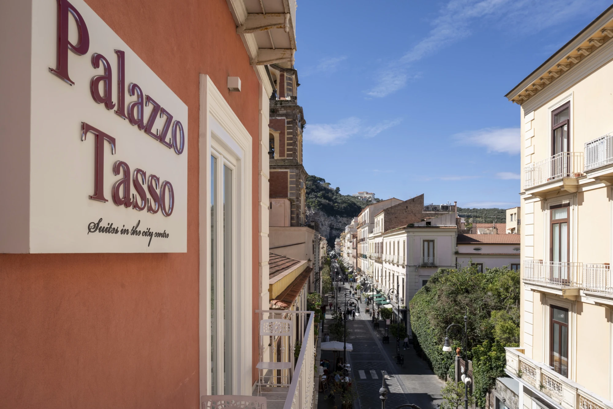 Vista della facciata di Palazzo Tasso e di una strada cittadina soleggiata.