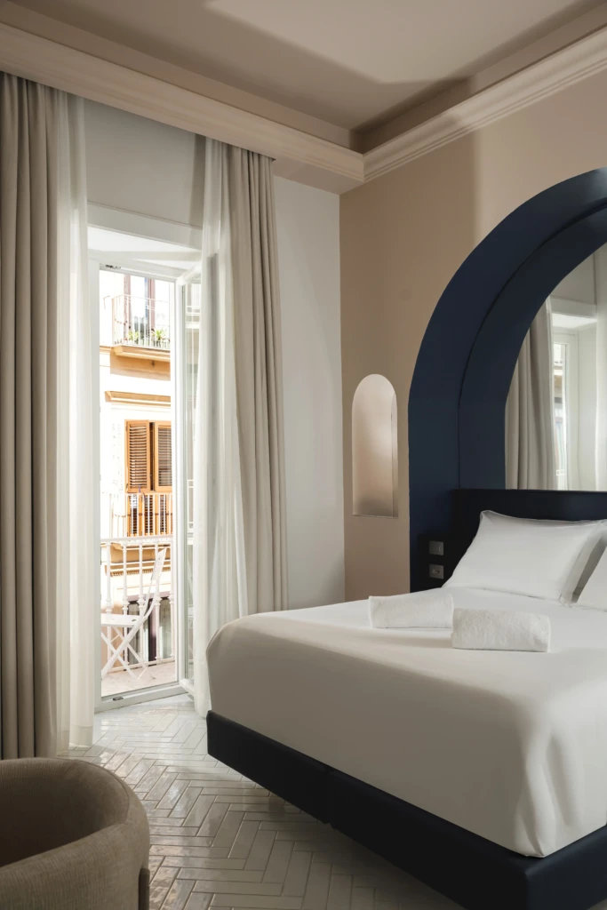 Camera moderna con letto matrimoniale e finestra aperta su un balcone.