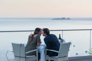 A couple leans in close at a table overlooking the ocean.