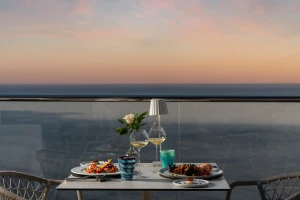 A table for two with dinner set on a balcony overlooking a sunset view.