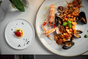 A plate of seafood pasta with shellfish and a prawn, alongside a small dessert.