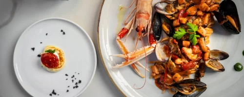 Un piatto di spaghetti ai frutti di mare con scampi e una piccola porzione di formaggio o dessert su un piatto separato.