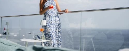 Donna elegante con abito estivo che beve un aperitivo su una terrazza con vista sul mare.