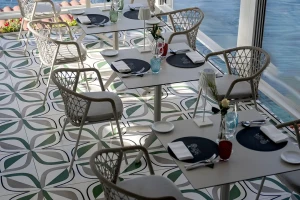 A seaside restaurant with patterned tile flooring and set tables overlooking the ocean.