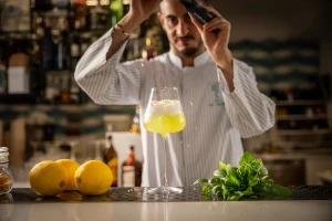 A bartender garnishing a yellow cocktail with lemons and basil on the counter.