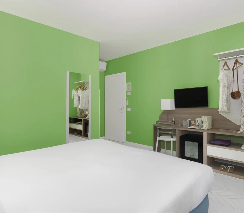 Camera da letto moderna con pareti verde chiaro, letto bianco e TV a schermo piatto.
