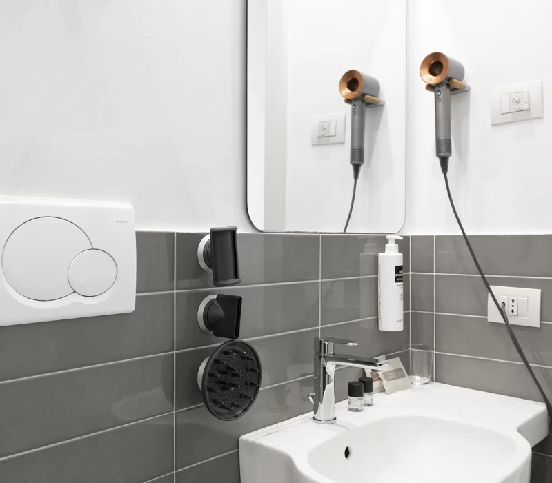 Bagno moderno con lavabo bianco, rivestimento in piastrelle grigie e accessori da toilette.
