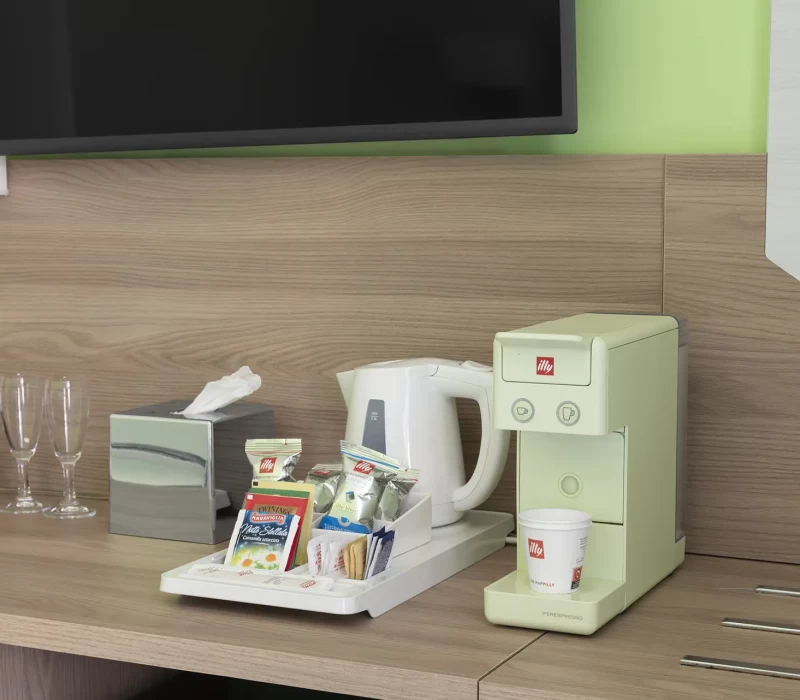 Macchinetta del caffè con tazza e accessori su un tavolo di legno.