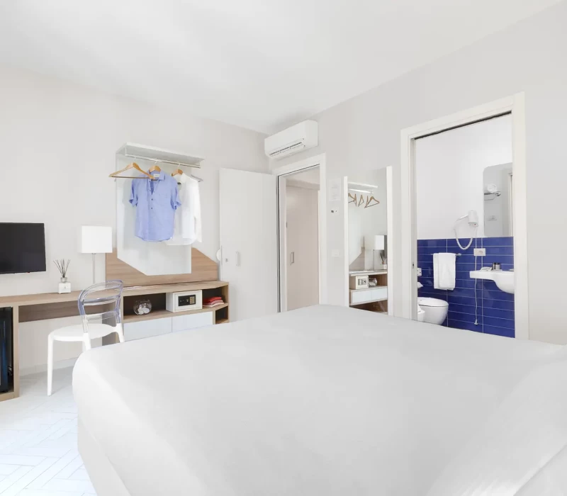 Camera d'albergo moderna con letto, TV, armadio aperto e bagno privato.