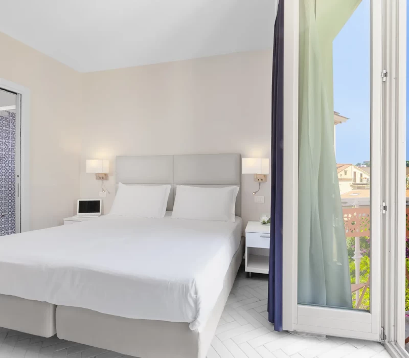 Camera da letto luminosa con letto matrimoniale, bagno blu e balcone.