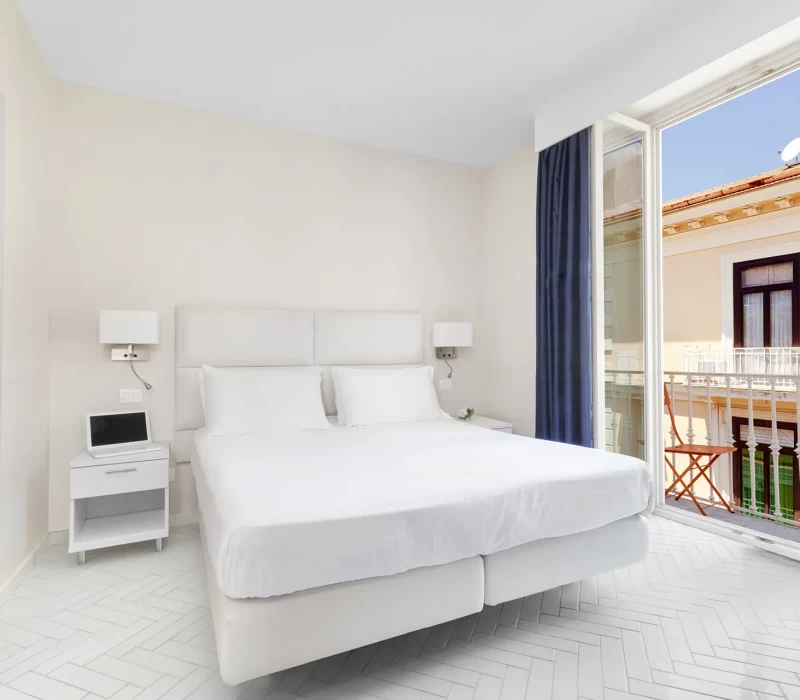 Camera da letto moderna con letto matrimoniale, bagno annesso e balcone con vista esterna.