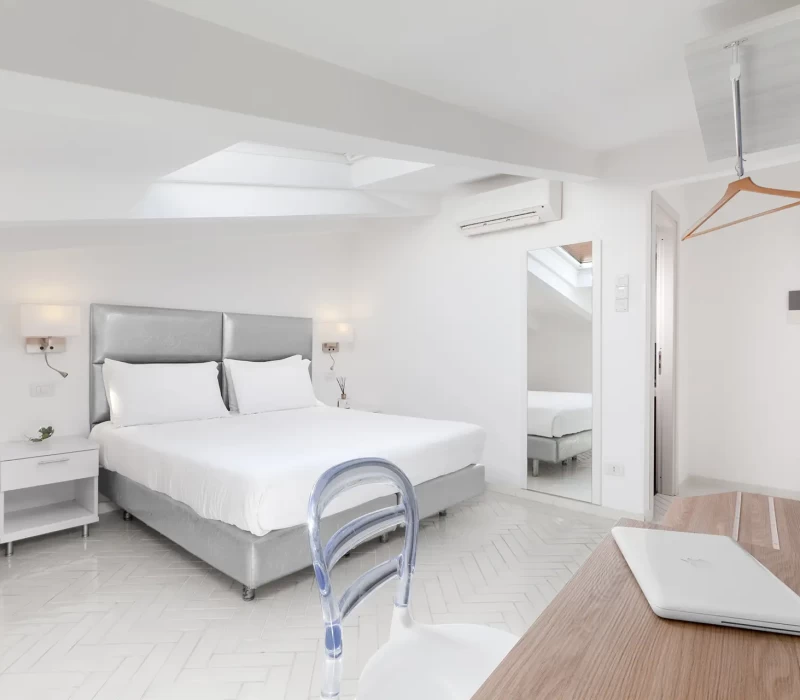 Camera da letto moderna e luminosa con letto matrimoniale, scrivania e specchio a parete.