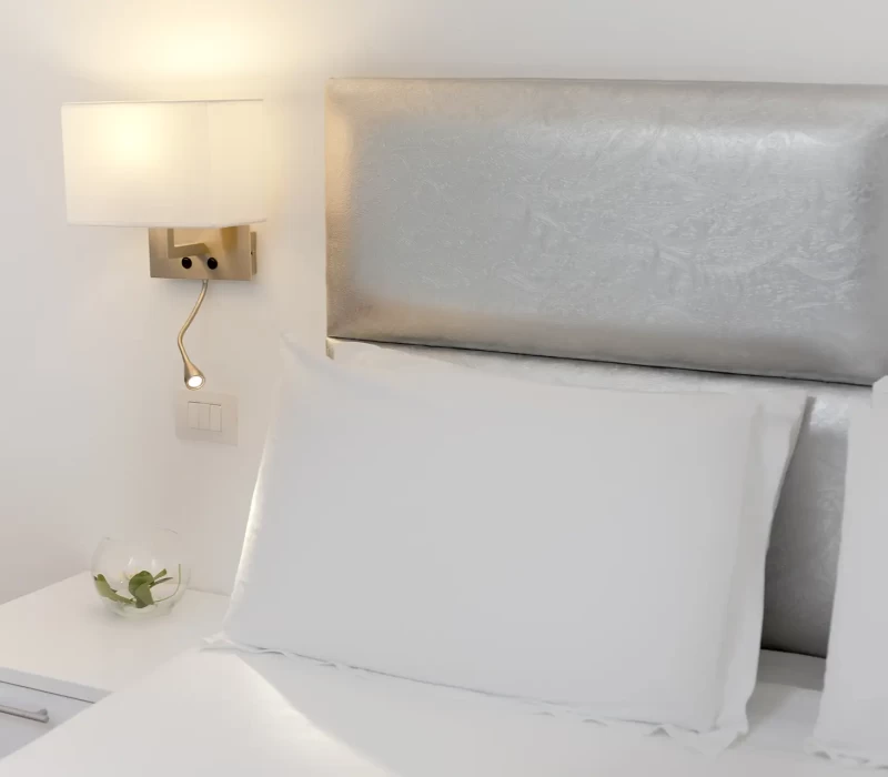 Testiera del letto moderna con lampada da parete e comodino bianco.