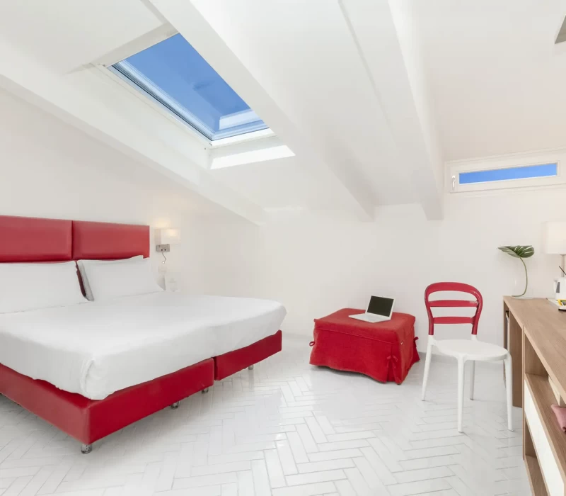 Camera da letto moderna con arredi bianchi e rossi sotto un lucernario.