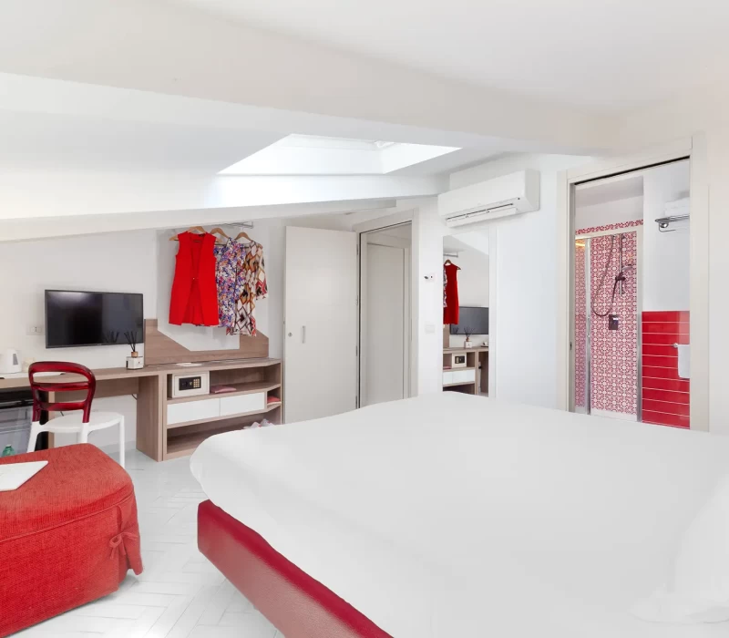 Camera da letto moderna con dettagli rossi e un bagno adiacente.