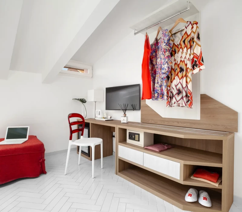 Spazio di lavoro moderno con scrivania in legno, sedia, laptop e abiti appesi.