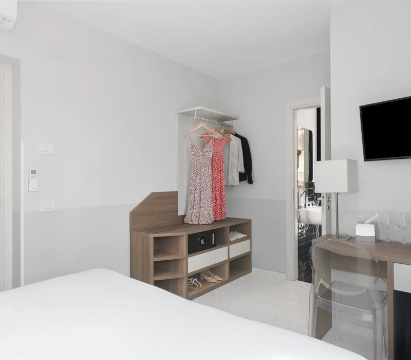 Camera d'albergo moderna con abiti appesi, televisione e minibar.