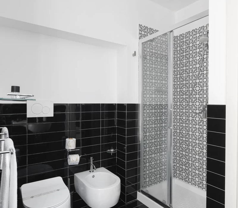 Bagno moderno con piastrelle nere lucide e doccia con vetro decorato.