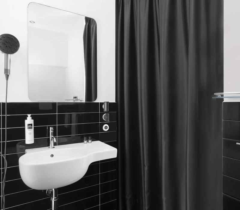 Bagno moderno con lavandino bianco, specchio e tenda doccia nera.