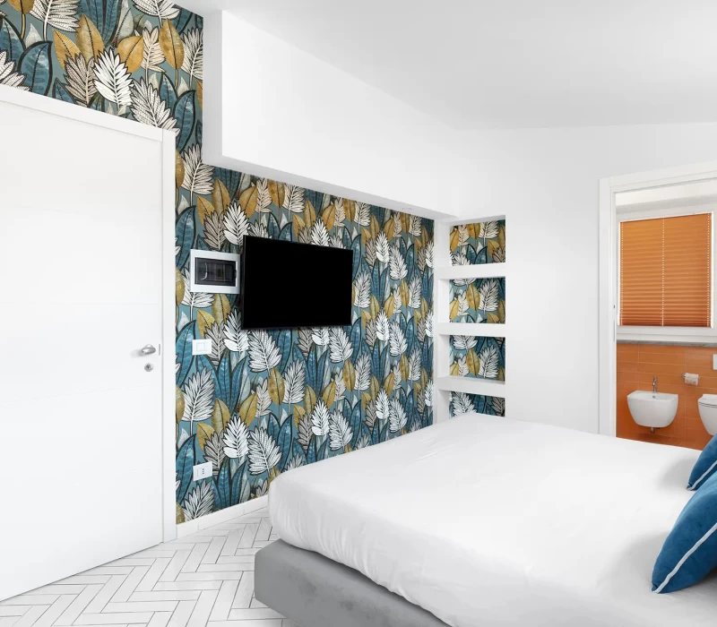 Camera da letto moderna con carta da parati a motivo tropicale e televisore a parete.