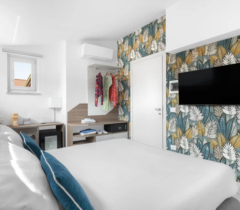 Camera d'albergo luminosa e moderna con letto matrimoniale, carta da parati floreale e TV a parete.