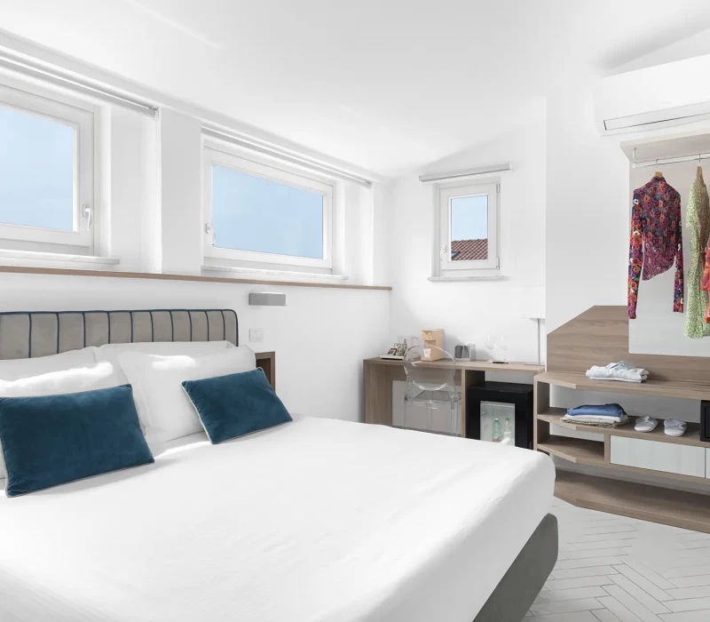 Camera da letto luminosa e moderna con letto matrimoniale, tre finestre e un armadio a vista.