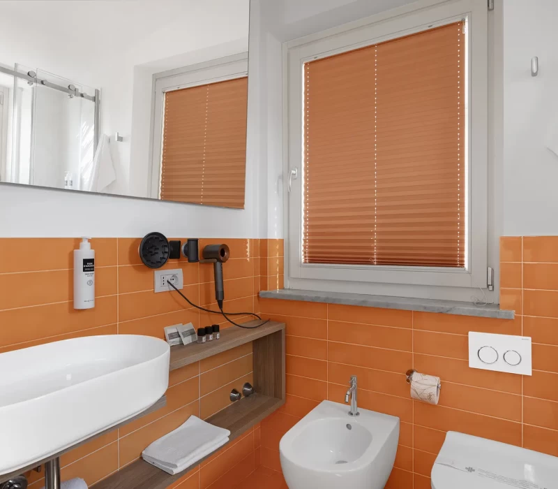 Bagno moderno con piastrelle arancioni, lavandino bianco, bidet e accessori.