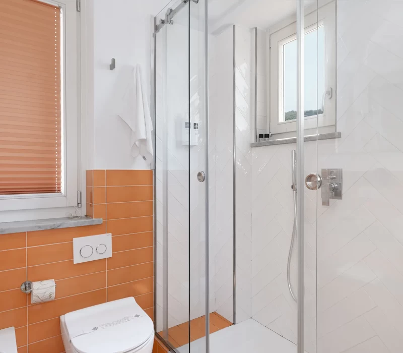 Bagno moderno con piastrelle arancioni e cabina doccia in vetro.