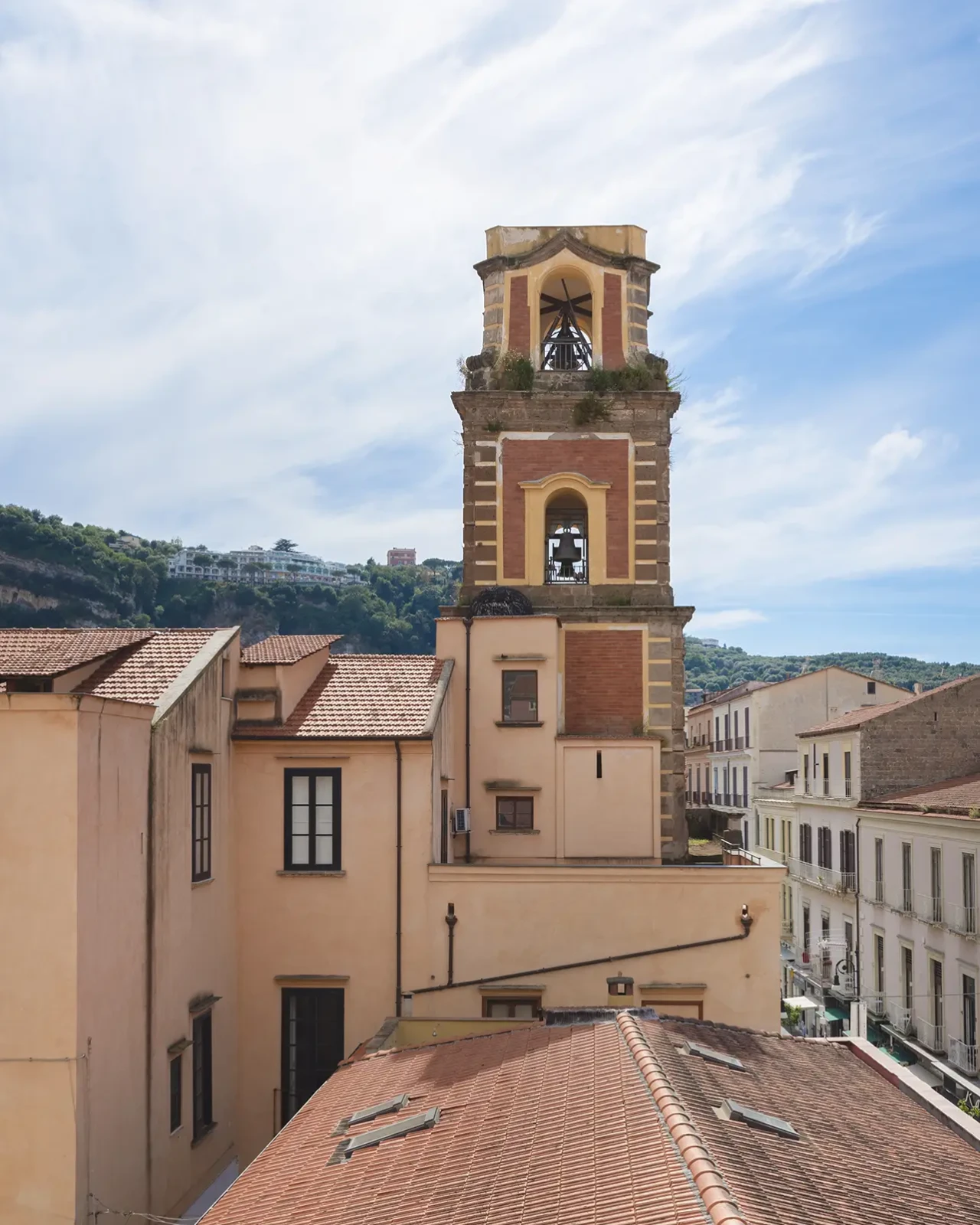 A tall bell tower stands among buildings under a blue sky.