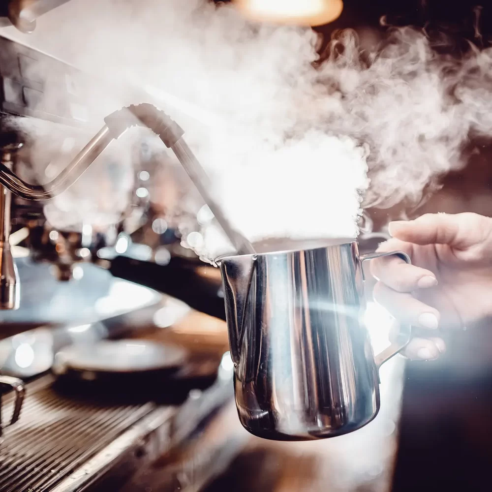 Una mano tiene una lattiera sotto una lancia a vapore per montare il latte.