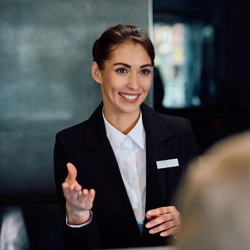 Donna sorridente in uniforme dietro un bancone di reception.